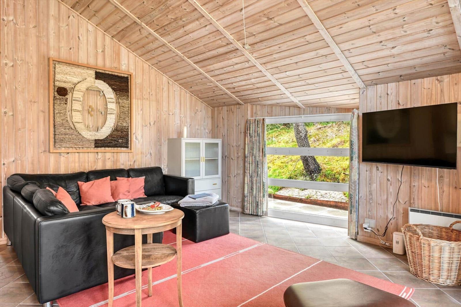 Wohnzimmer mit Sofa, Fernseher und Blick auf die Natur.