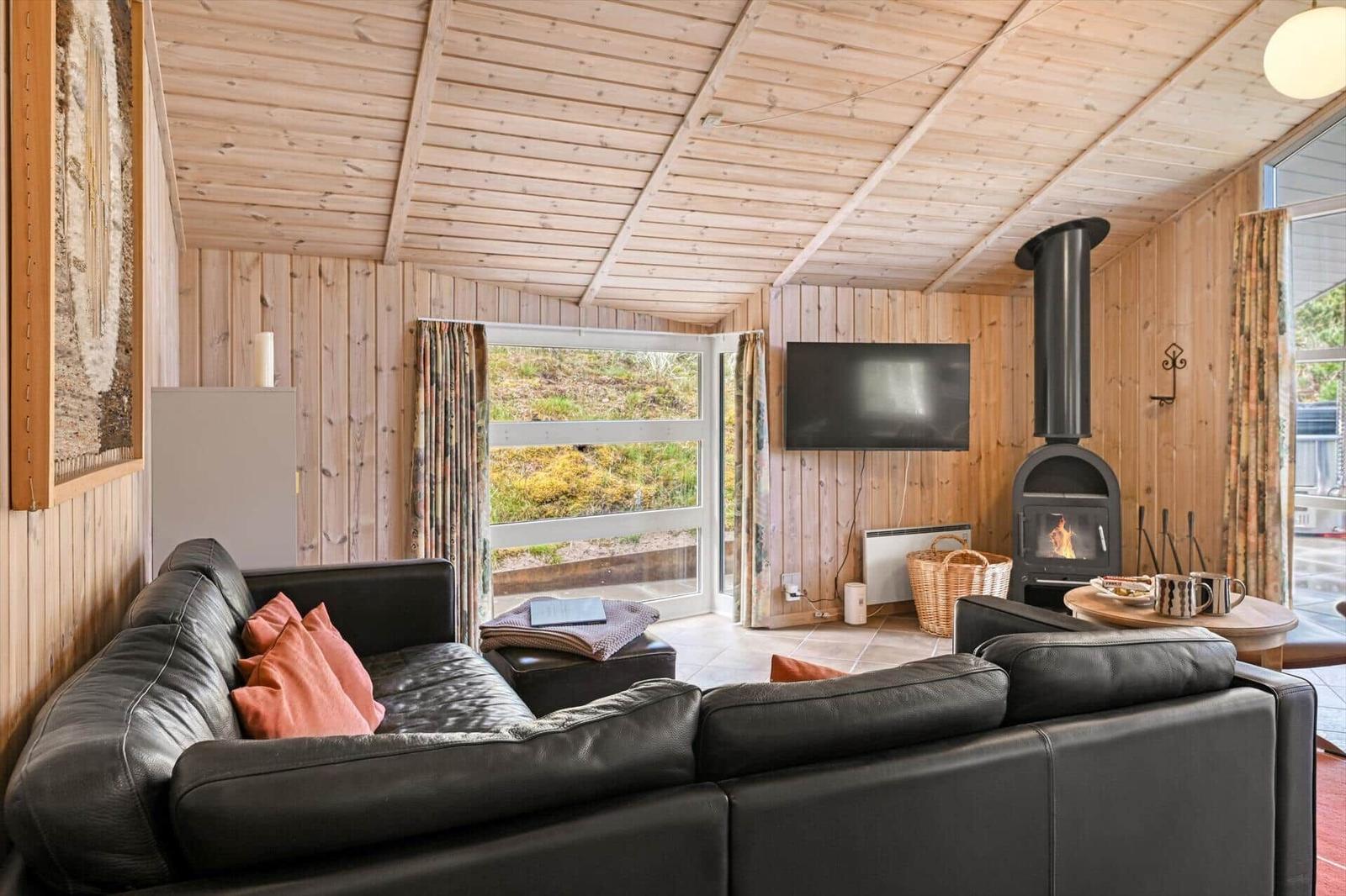 Wohnzimmer mit Sofa, Kamin und TV. Holzwände und -decke. Blick auf Garten.