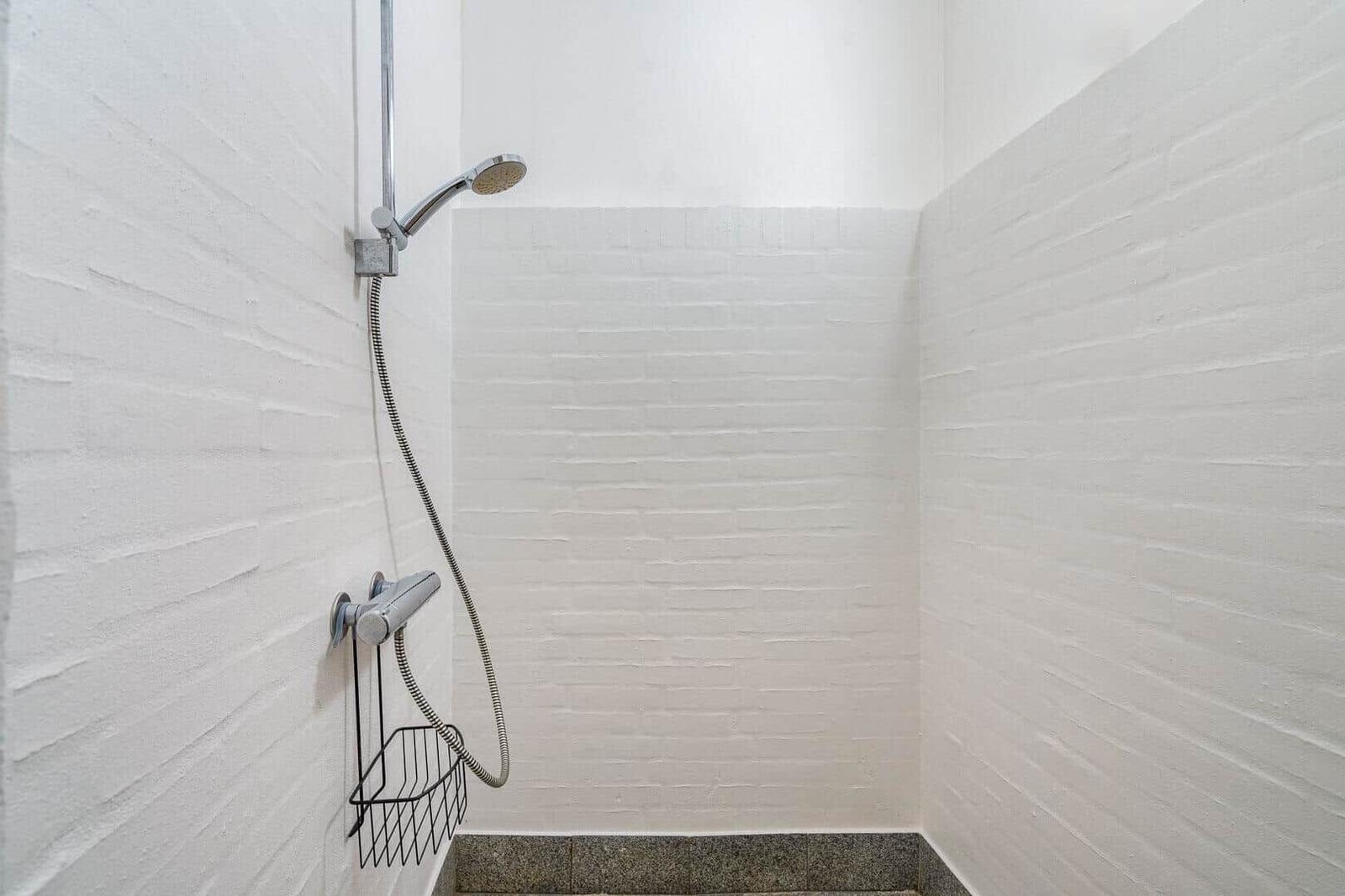 Dusche mit Handbrause und Ablagekorb an weißer Wand
