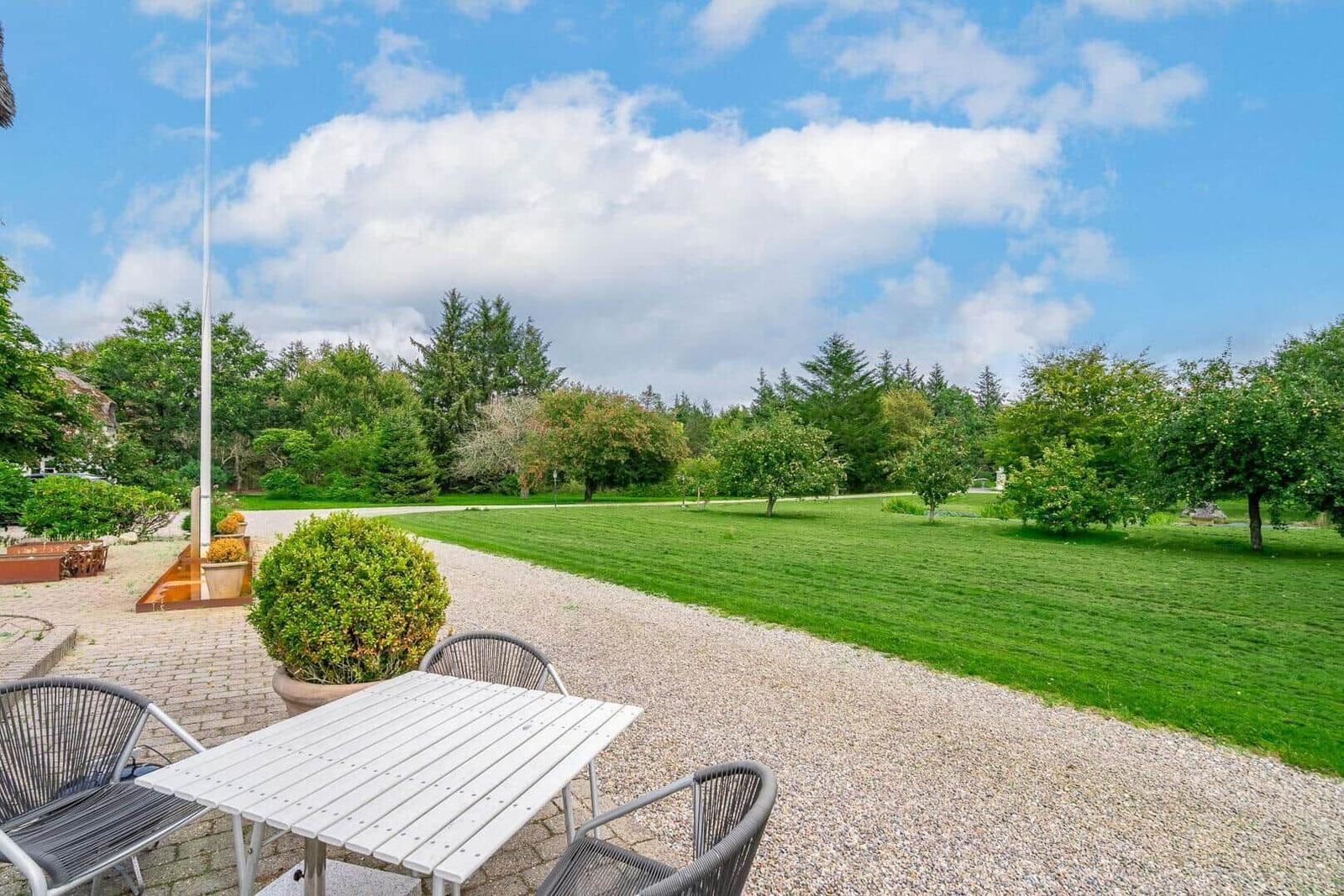Terrasse mit Tisch und Stühlen, Blick auf grünen Rasen und Bäume unter blauem Himmel.