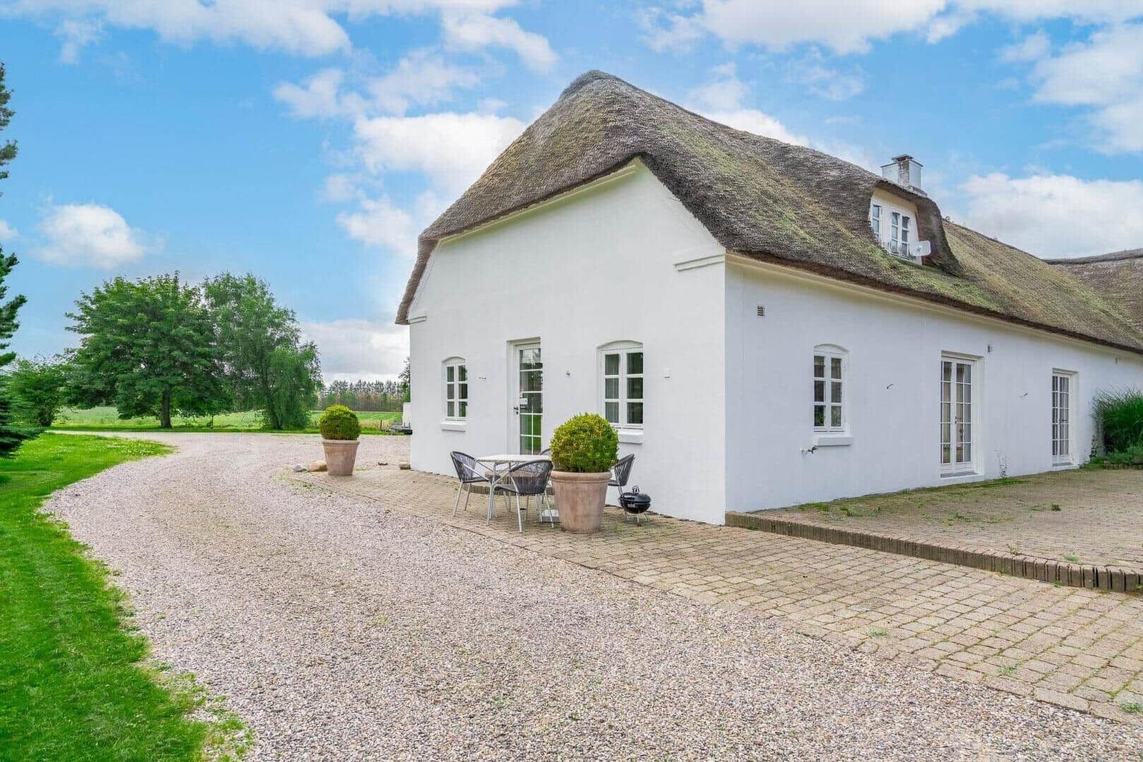Weißes Haus mit Strohdach, Gartenbereich und Tisch mit Stühlen.