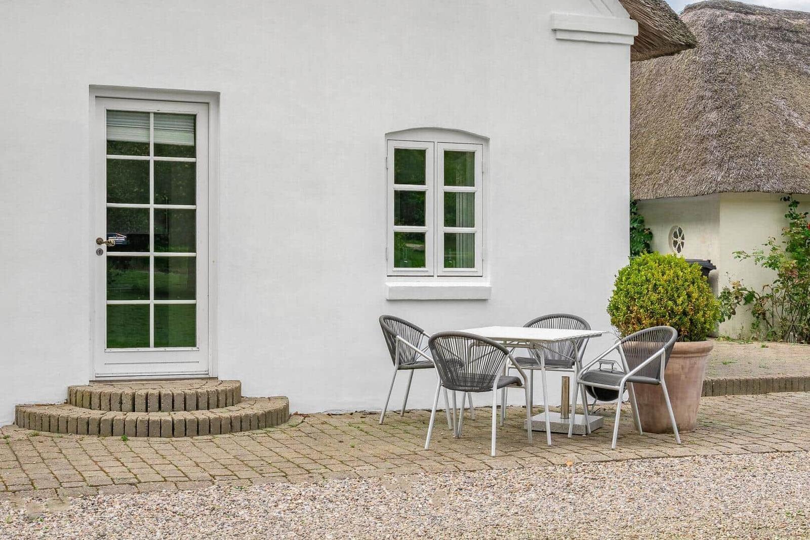 Haus mit weißer Fassade, Terrasse und Sitzgruppe. Thatched roof house im Hintergrund.