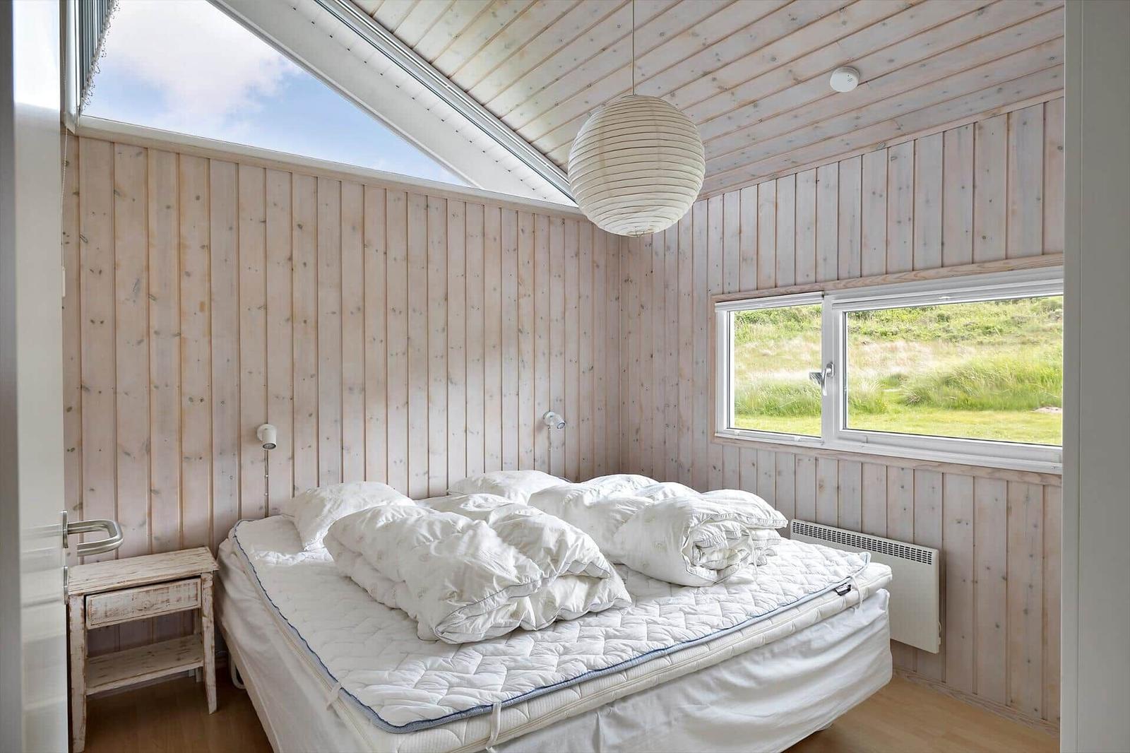 Schlafzimmer mit Holzwand, Bett und Fenster zum Grasland.