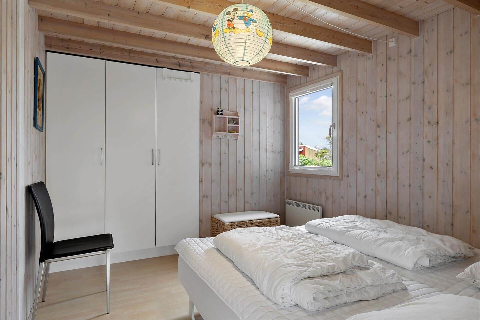Schlafzimmer mit Holzwand, Bett, Kleiderschrank und Fenster.
