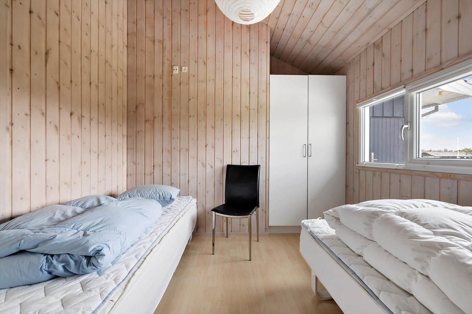 Zwei Betten, ein Schrank und ein Stuhl in einem Zimmer mit Holzwänden und Fenster.