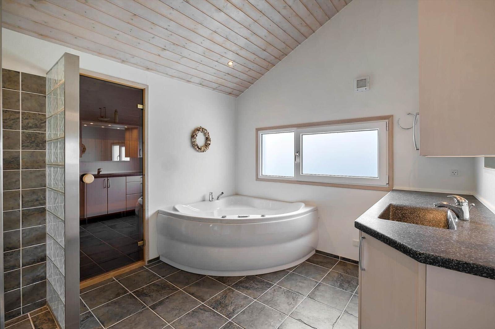 Badezimmer mit Dusche, Whirlpool und Fenster. Holzdecke und Fliesenboden.
