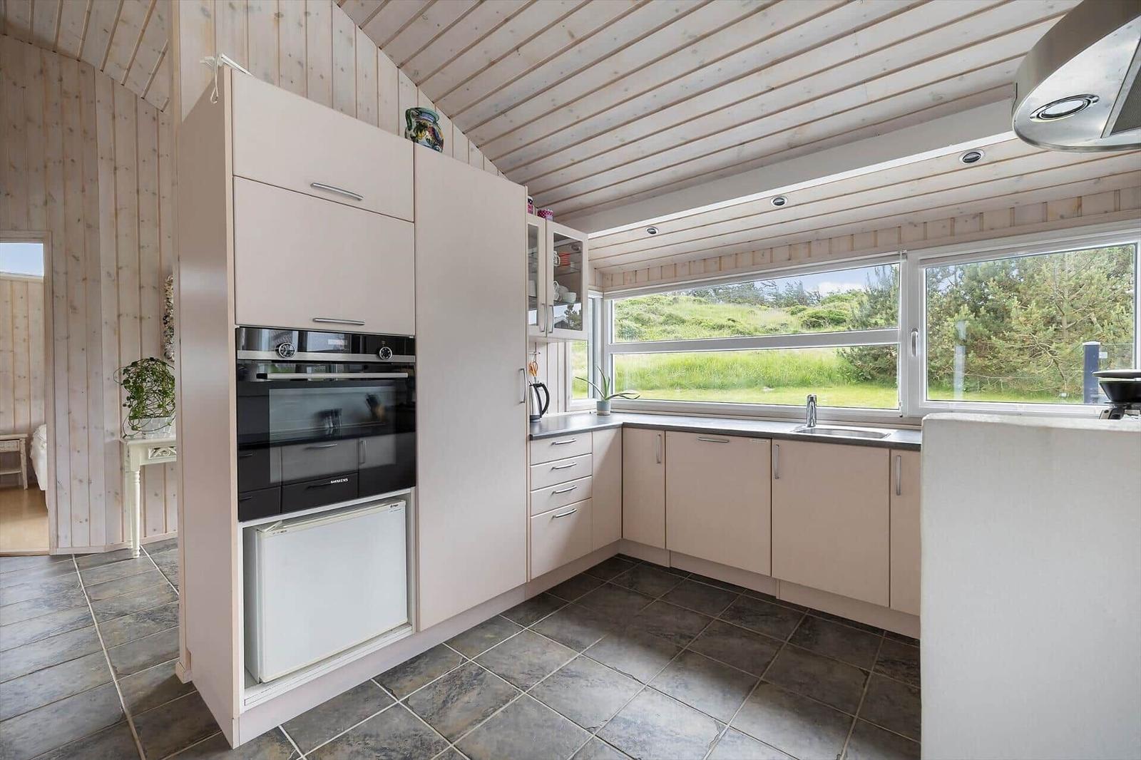 Küche mit hellen Schränken, Fenster mit Blick auf Grünfläche und integrierte Spüle.