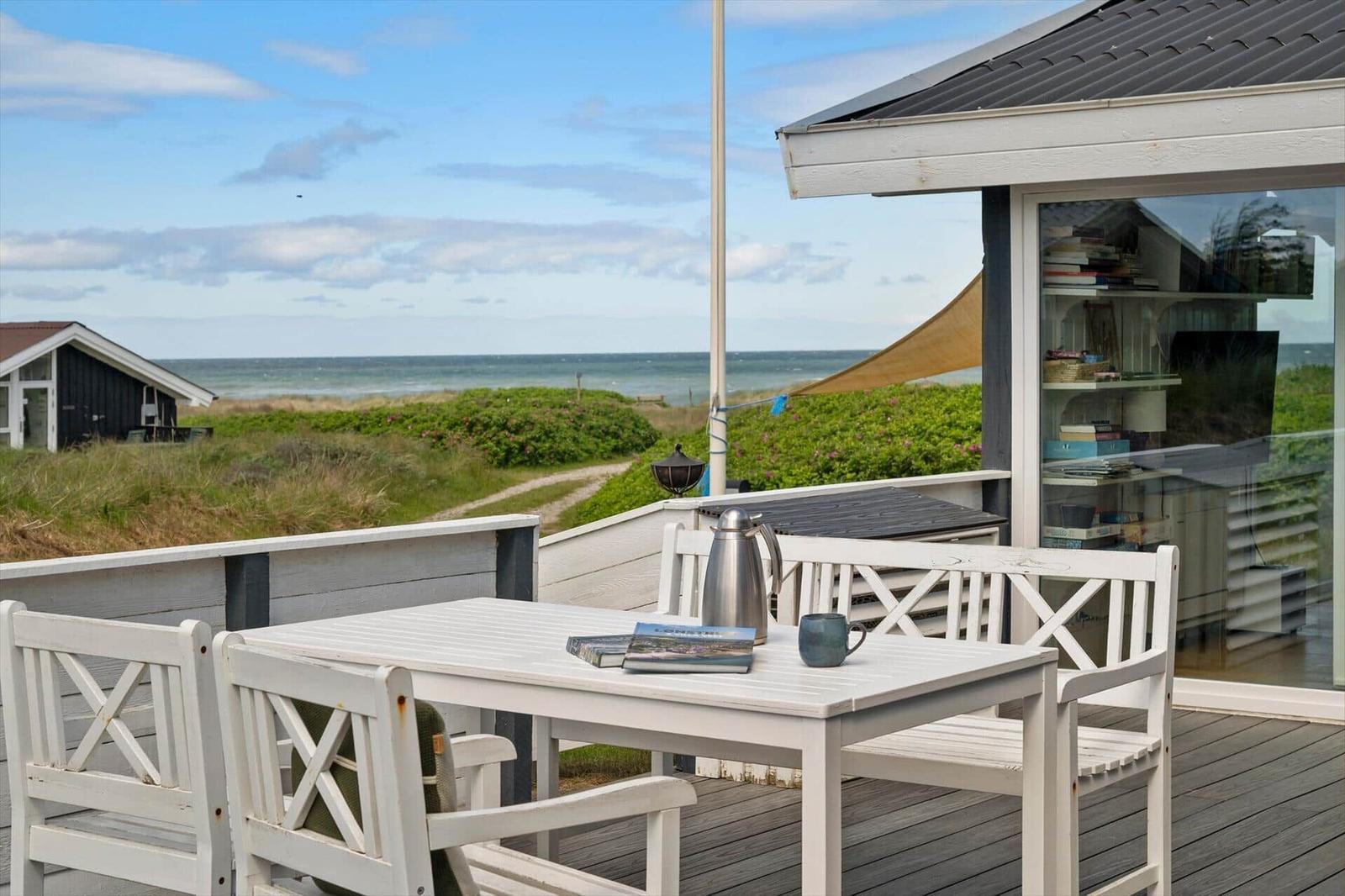 Terrasse mit weißem Tisch und Stühlen, Blick auf Strand und Meer.