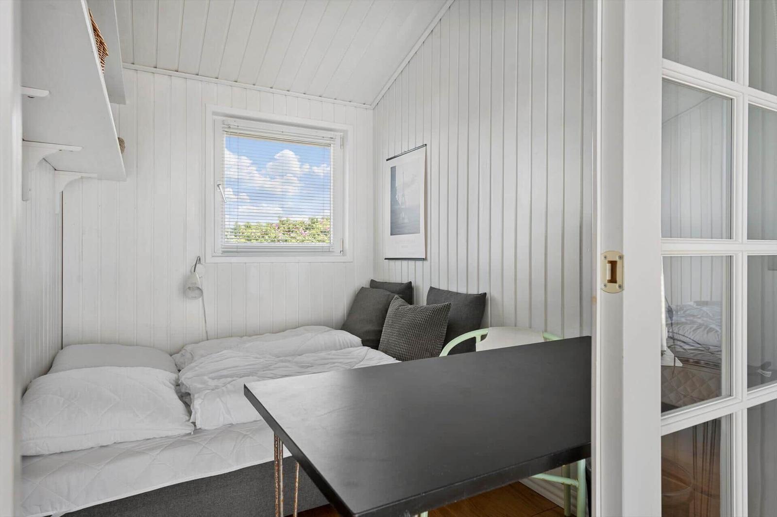 Zimmer mit Bett, Tisch und Fenster mit Blick auf Grün.