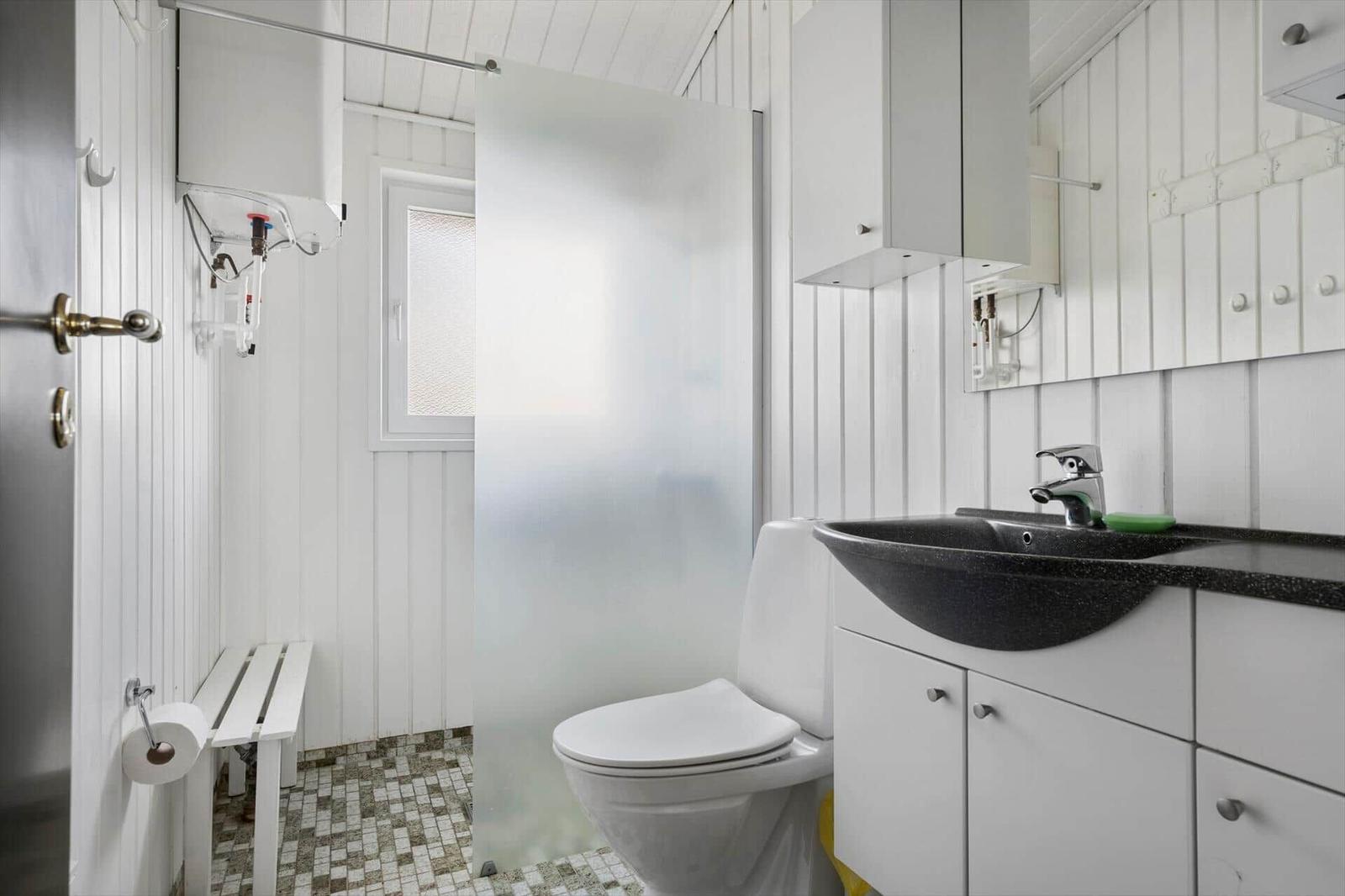 Badezimmer mit Toilette, Dusche und Waschbecken. Weiße Holzwandverkleidung und Mosaikfliesenboden.