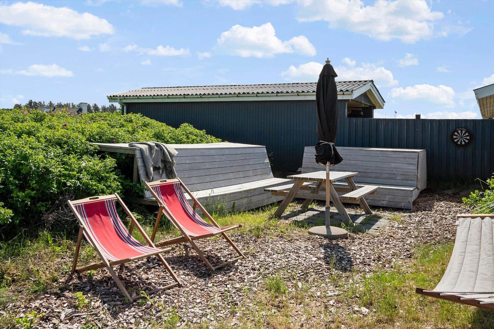Hinterhof mit Liegestühlen, Picknicktisch und Schirm. Hintergrund: Holzhaus und Zaun.