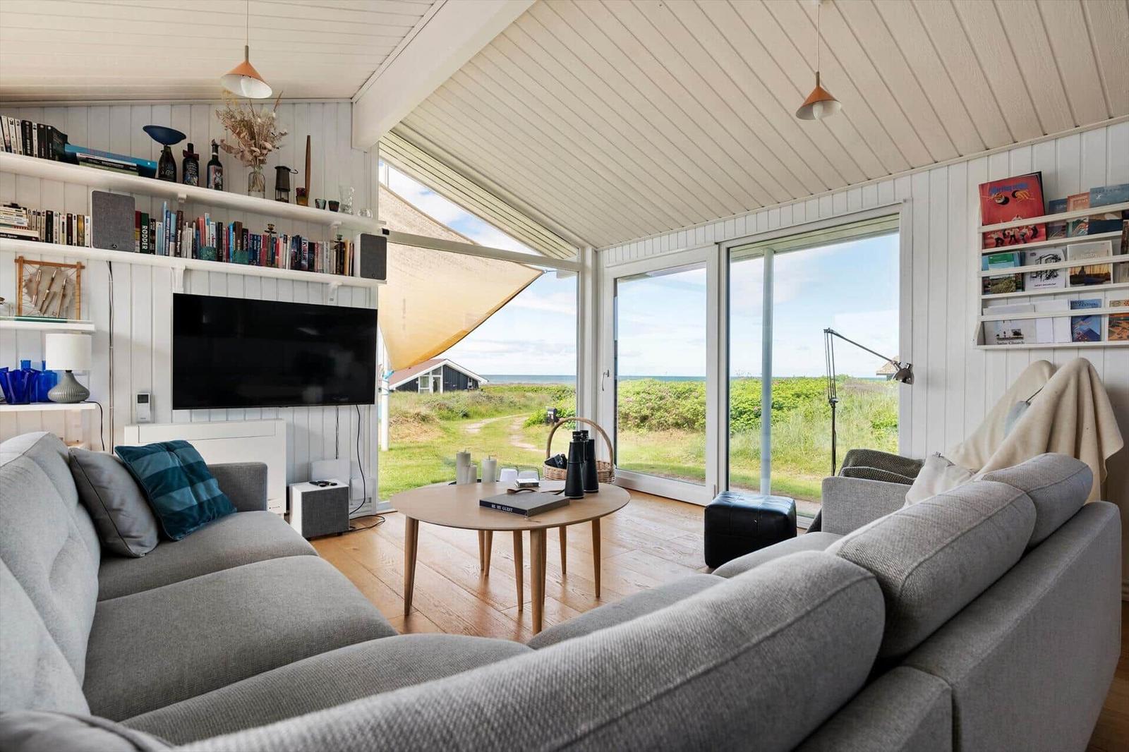 Wohnzimmer mit Sofa, Fernseher und Blick auf die Landschaft.