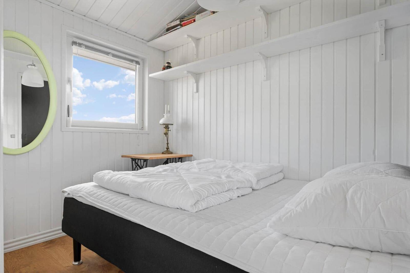Schlafzimmer mit weißer Holzwand, Bett und Fenster zum Himmel.