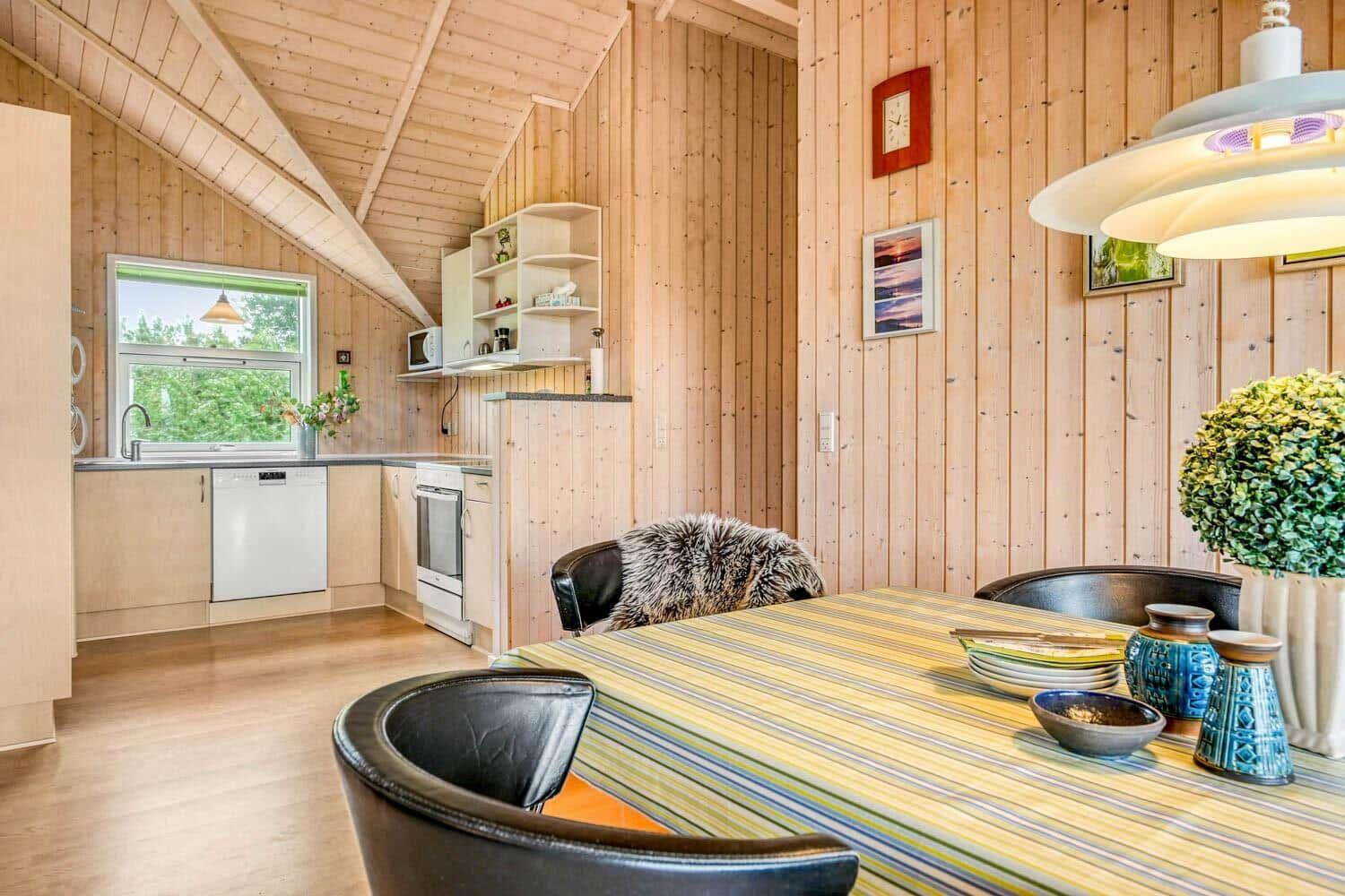 Küche und Essbereich mit Holzwand und -decke, Esstisch mit Stühlen und Fenster.