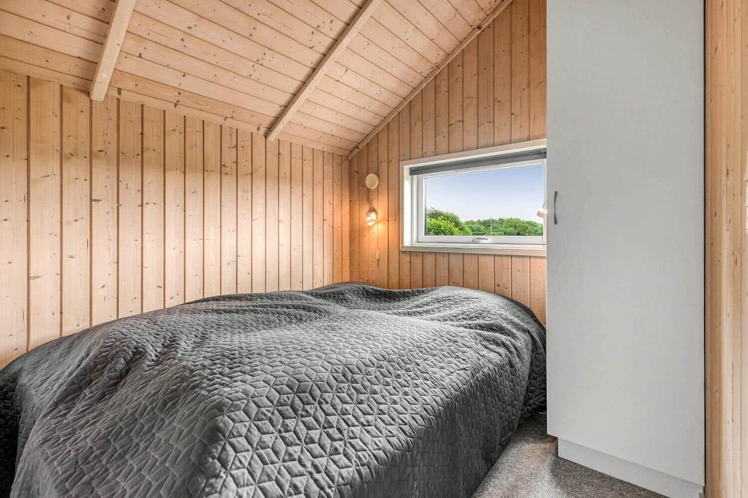 Schlafzimmer mit Holzwand, Bett und Fenster mit Blick auf Grün.