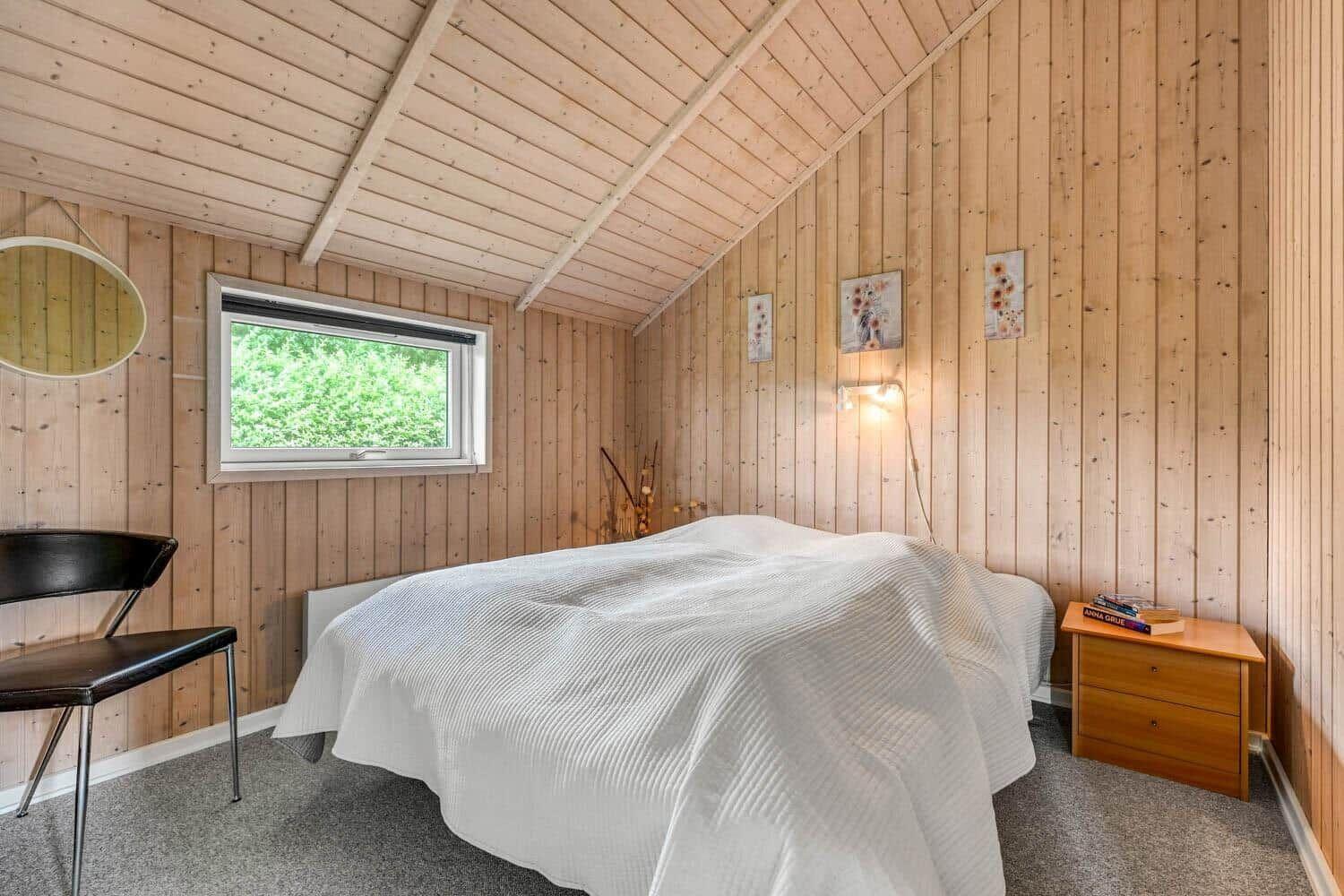 Schlafzimmer mit Holzwänden, Bett, Nachttisch und Fenster.
