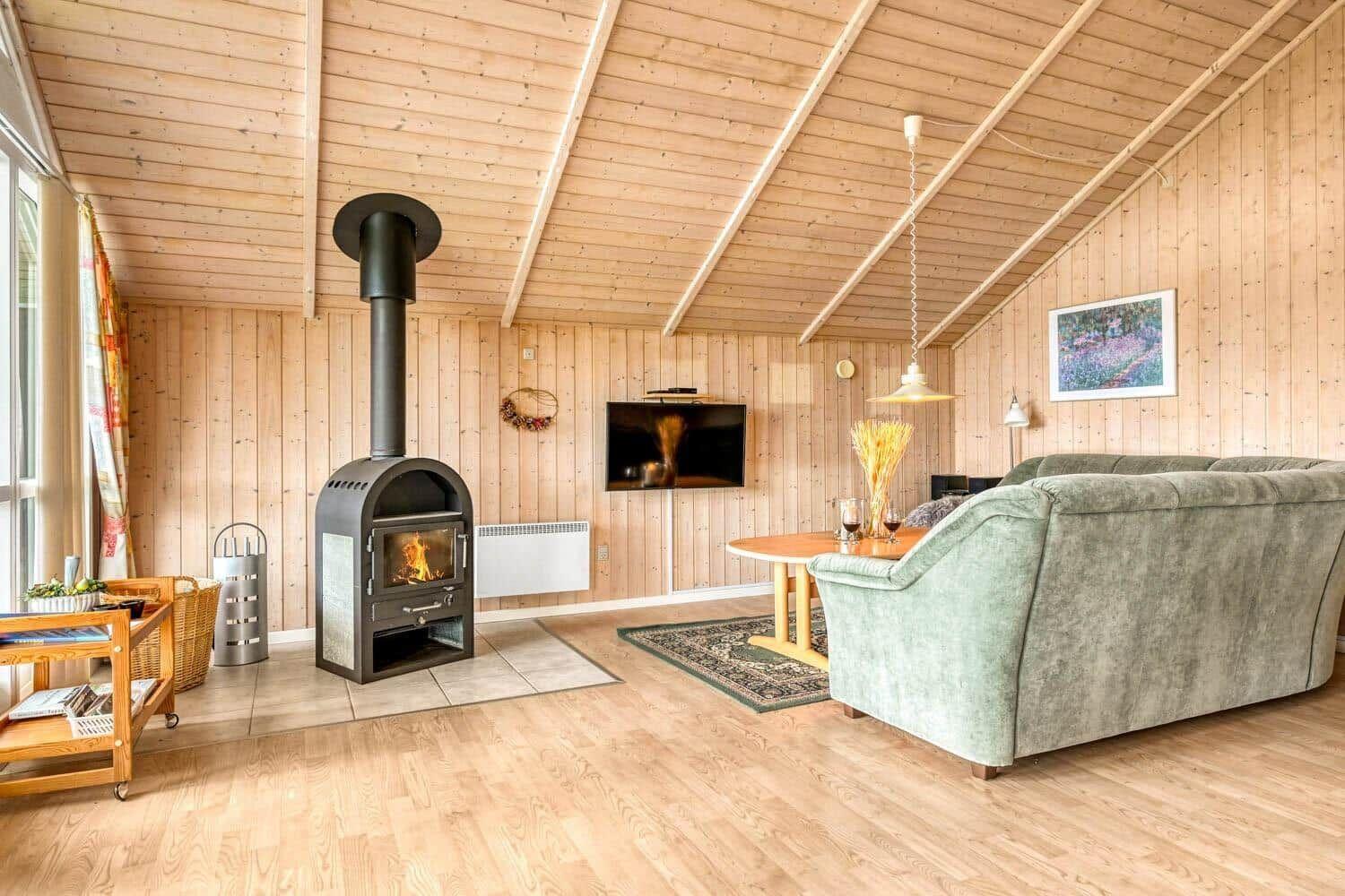 Wohnzimmer mit Kaminofen, Sofa und Fernseher an Holzwand
