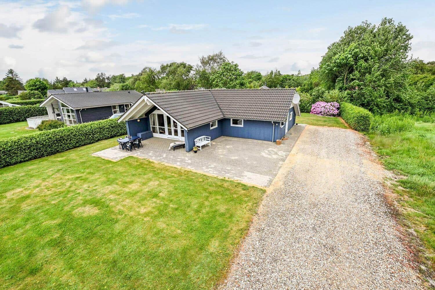 Blau gestrichenes Ferienhaus mit Terrasse und Garten. Gravelweg führt zum Eingang.