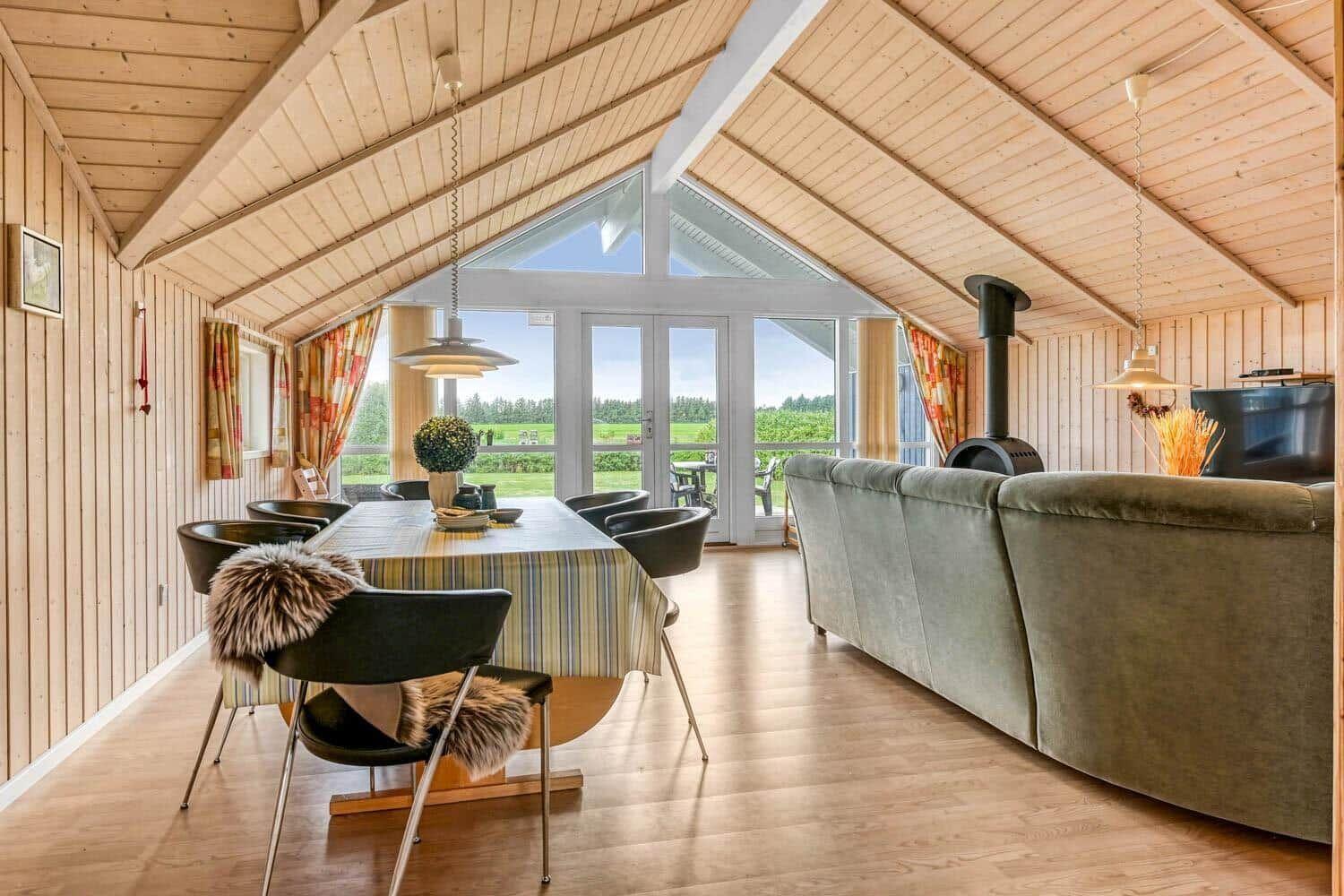 Ein Essbereich mit Tisch und Stühlen neben einem Sofa. Durchgehende Glasfront mit Blick auf die Landschaft.