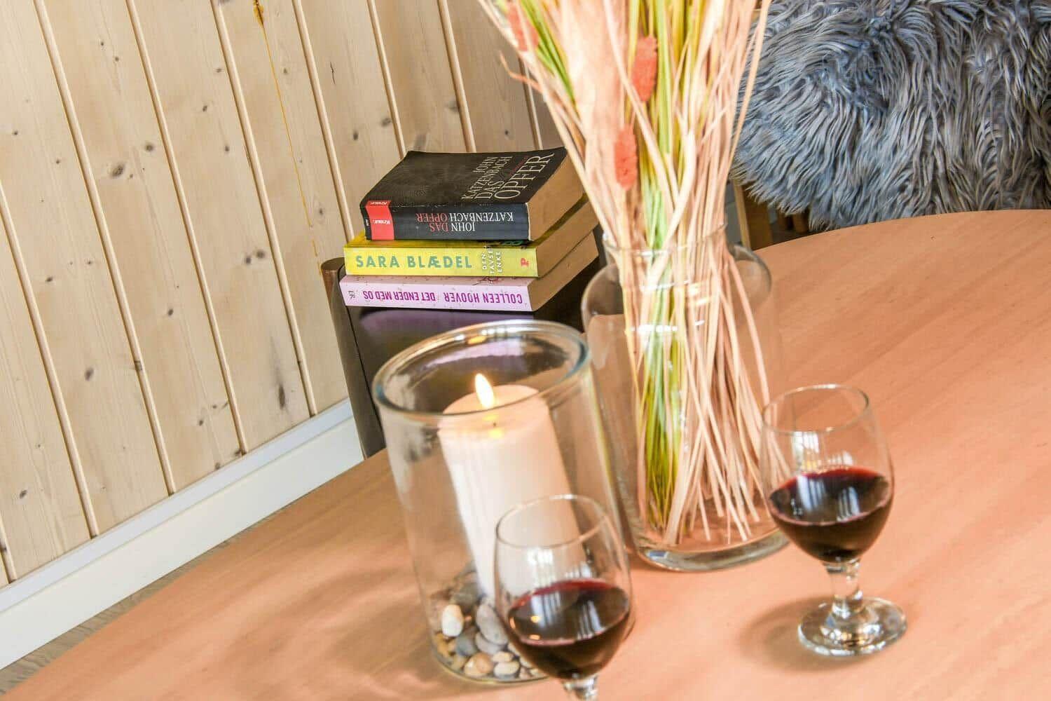 Tisch mit zwei Weingläsern, Kerze und Blumenstrauß. Bücher stapeln sich im Hintergrund.