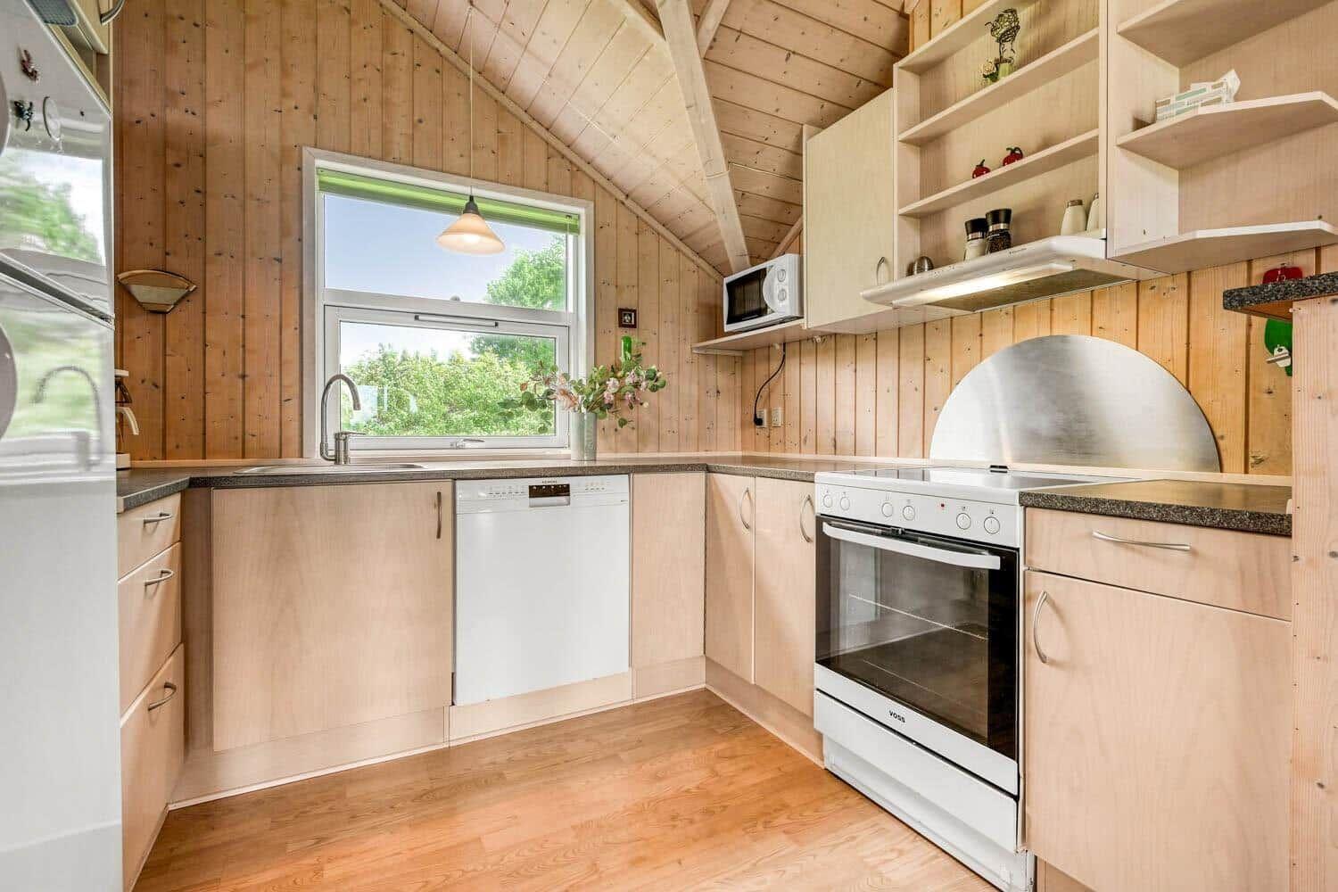 Küche mit Holzwänden, Spüle, Herd und Fenster mit Blick auf Grün.