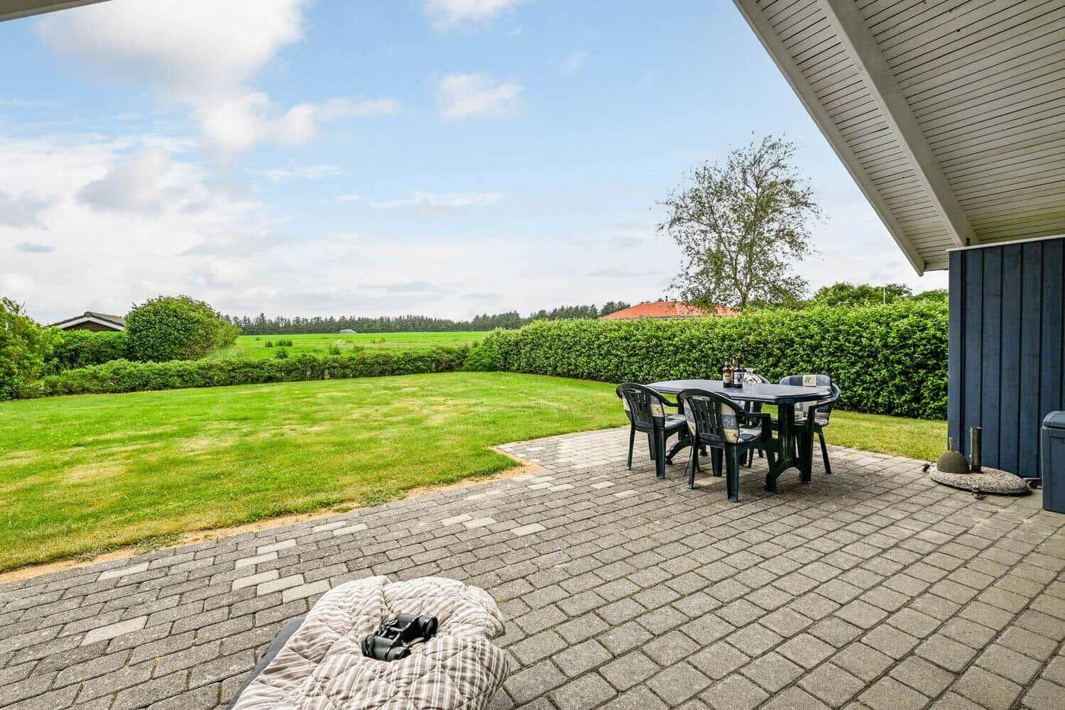 Terrasse mit Tisch und Stühlen, Blick auf grünen Rasen und Hecke.