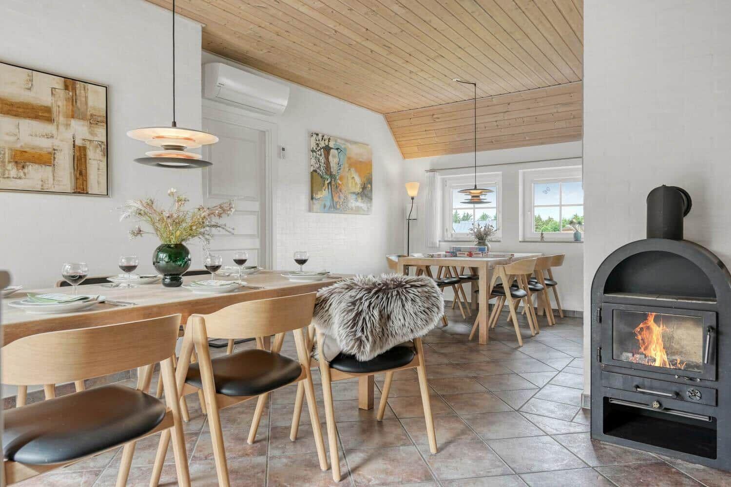 Essbereich mit Holztisch, Stühlen und Kaminofen. Holzdecke und Wandbilder sichtbar.