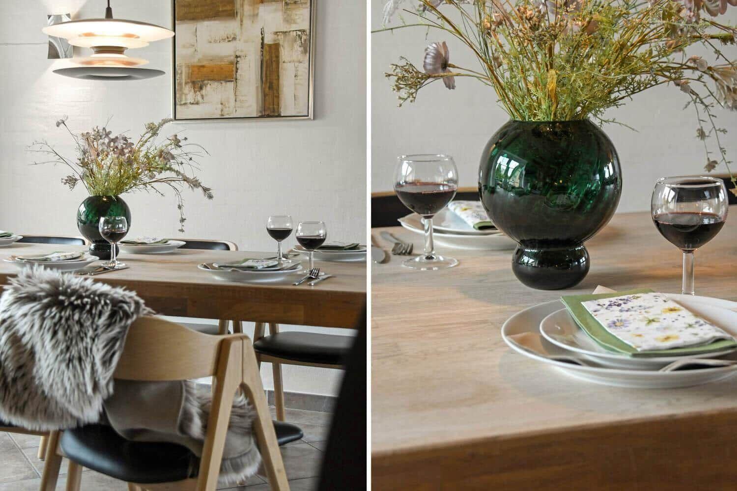 Esstisch mit Stühlen, Blumenvase und Weingläsern. Hintergrund: Wandbild und Deckenleuchte.