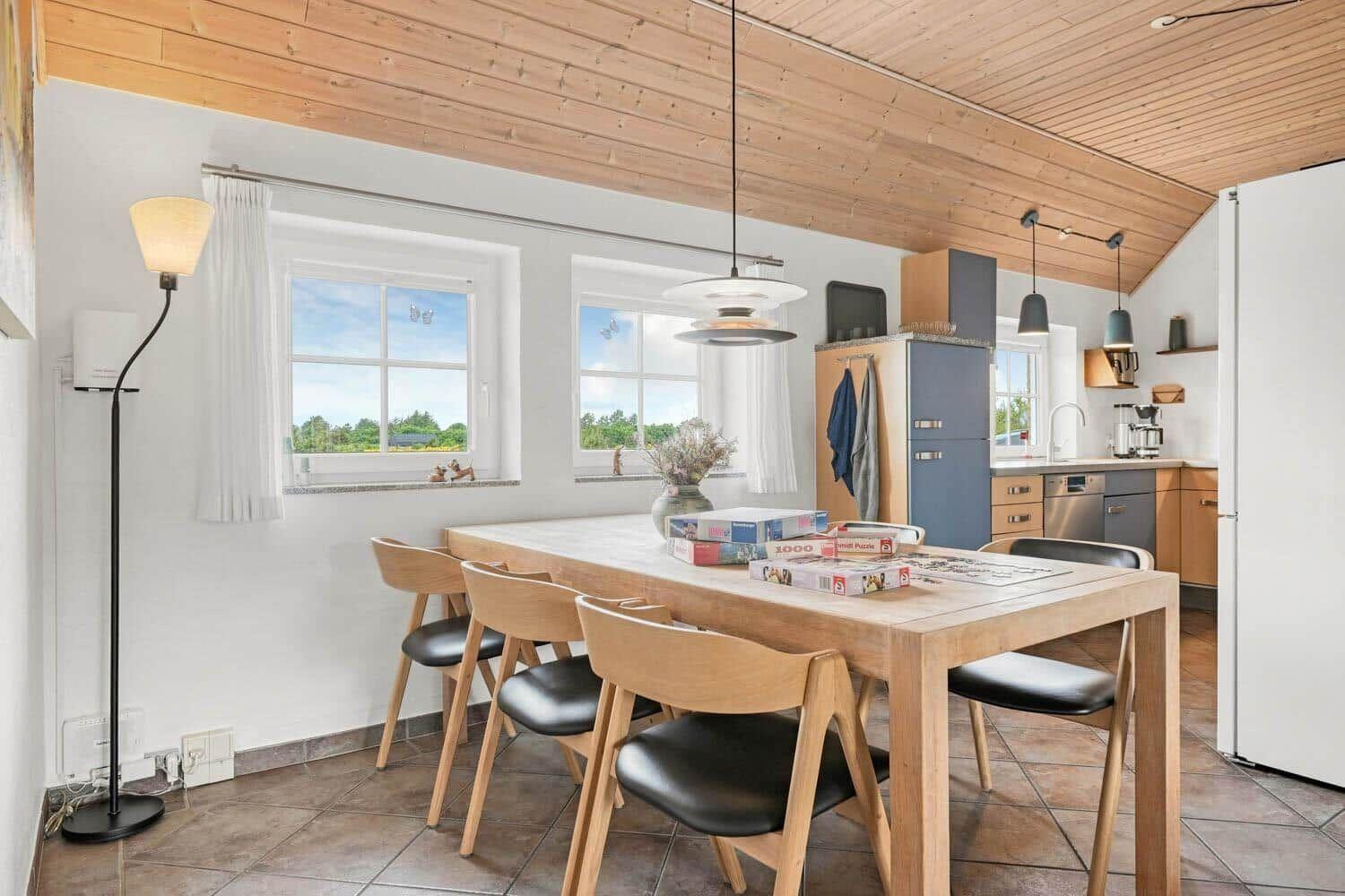 Essbereich mit Holztisch, Stühlen und Küchenbereich im Hintergrund.