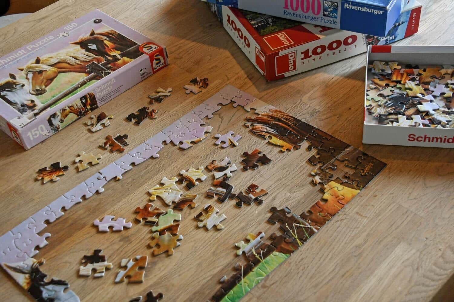 Puzzlestücke auf Holztisch. Mehrere Puzzles in verschiedenen Schwierigkeitsgraden.