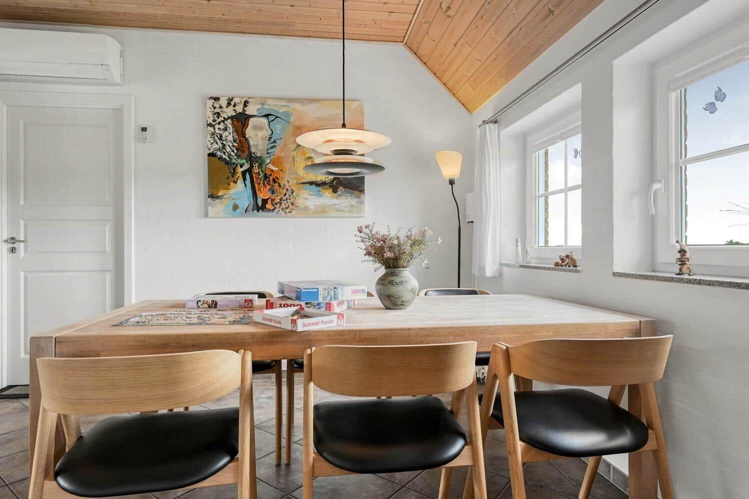 Esszimmer mit Holztisch, Stühlen und Wandbild. Fenster mit Blick nach draußen.