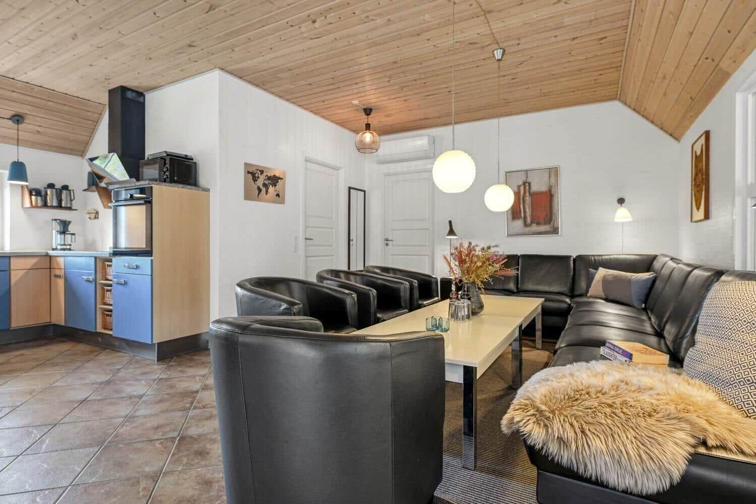 Wohnbereich mit Leder-Sofa, Esstisch und Küchenzeile unter Holzdecke.