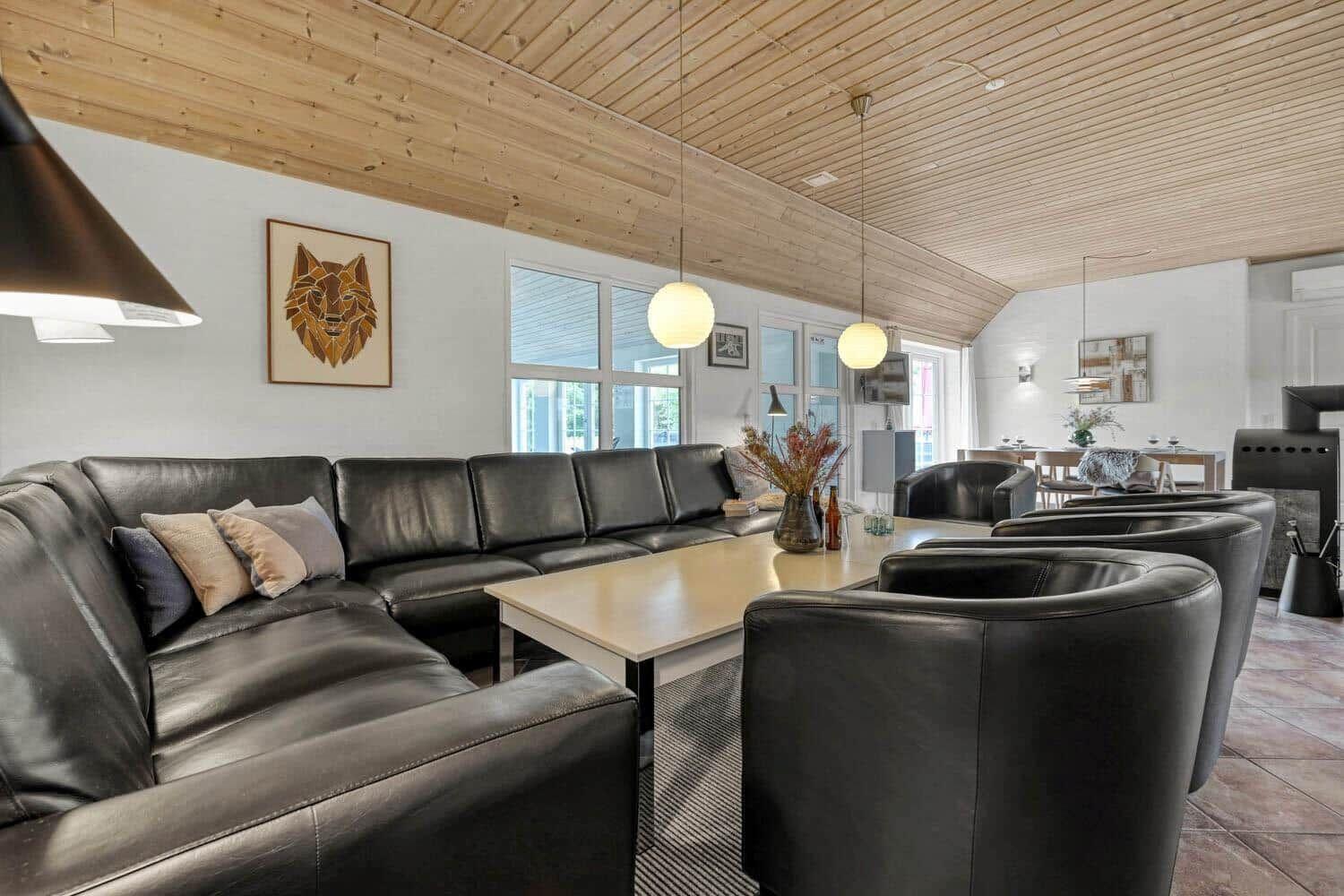 Wohnzimmer mit Ledersofa, Tisch und Sesseln. Holzdecke und Fenster sichtbar.