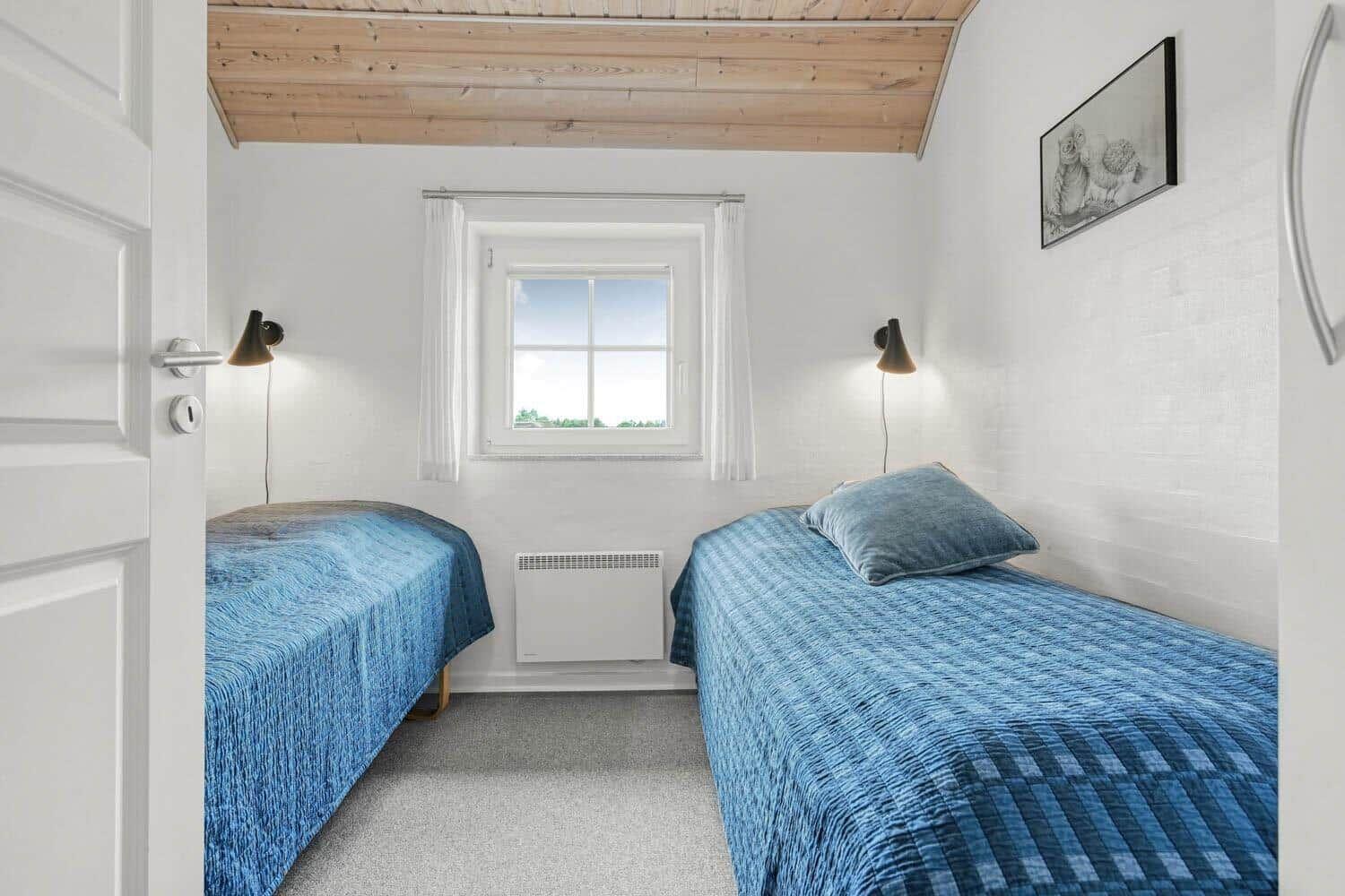 Zwei Betten mit blauen Bettdecken, Fenster und Decke aus Holz.