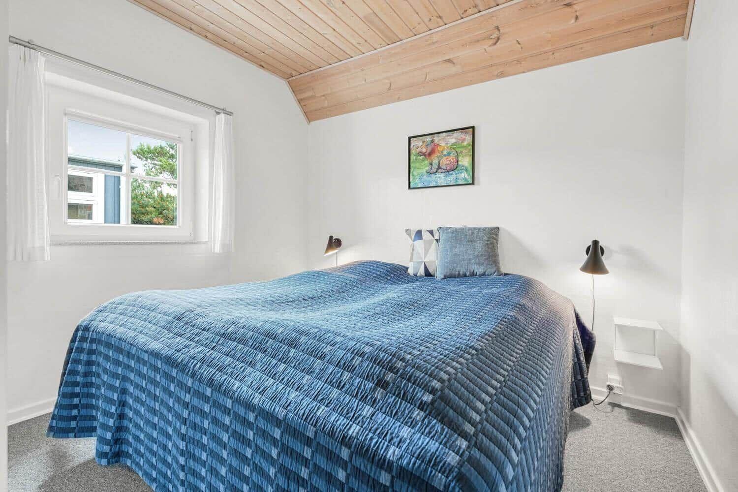 Schlafzimmer mit Bett, Fenster und Holzdecke.