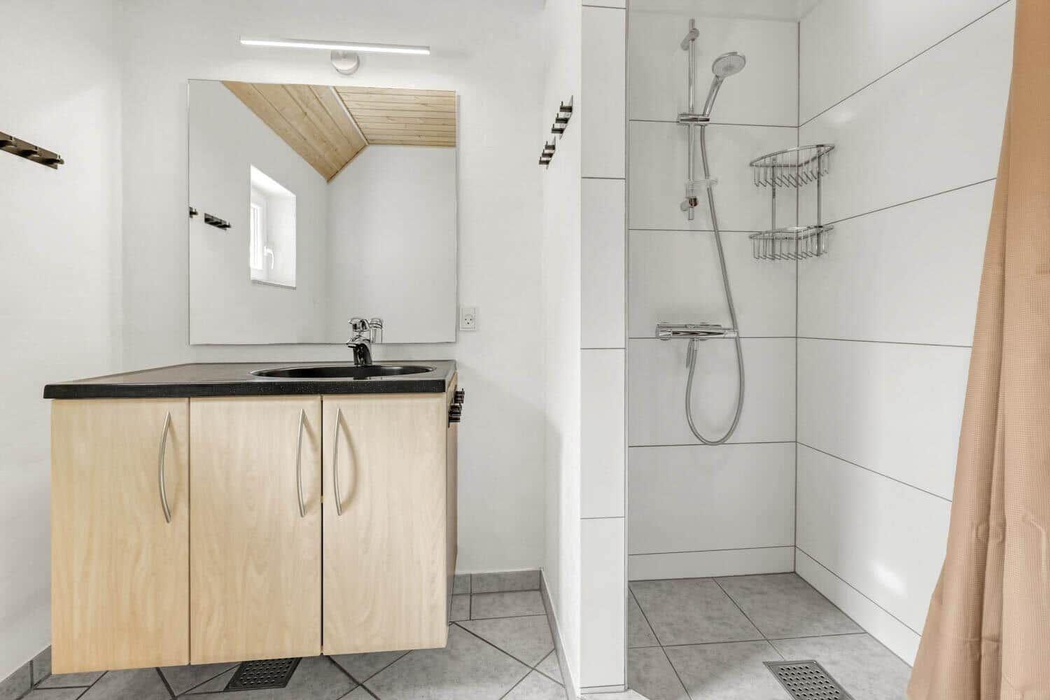 Bad mit Dusche, Waschbecken und Spiegelschrank. Weiße Fliesen und Holzoberflächen.