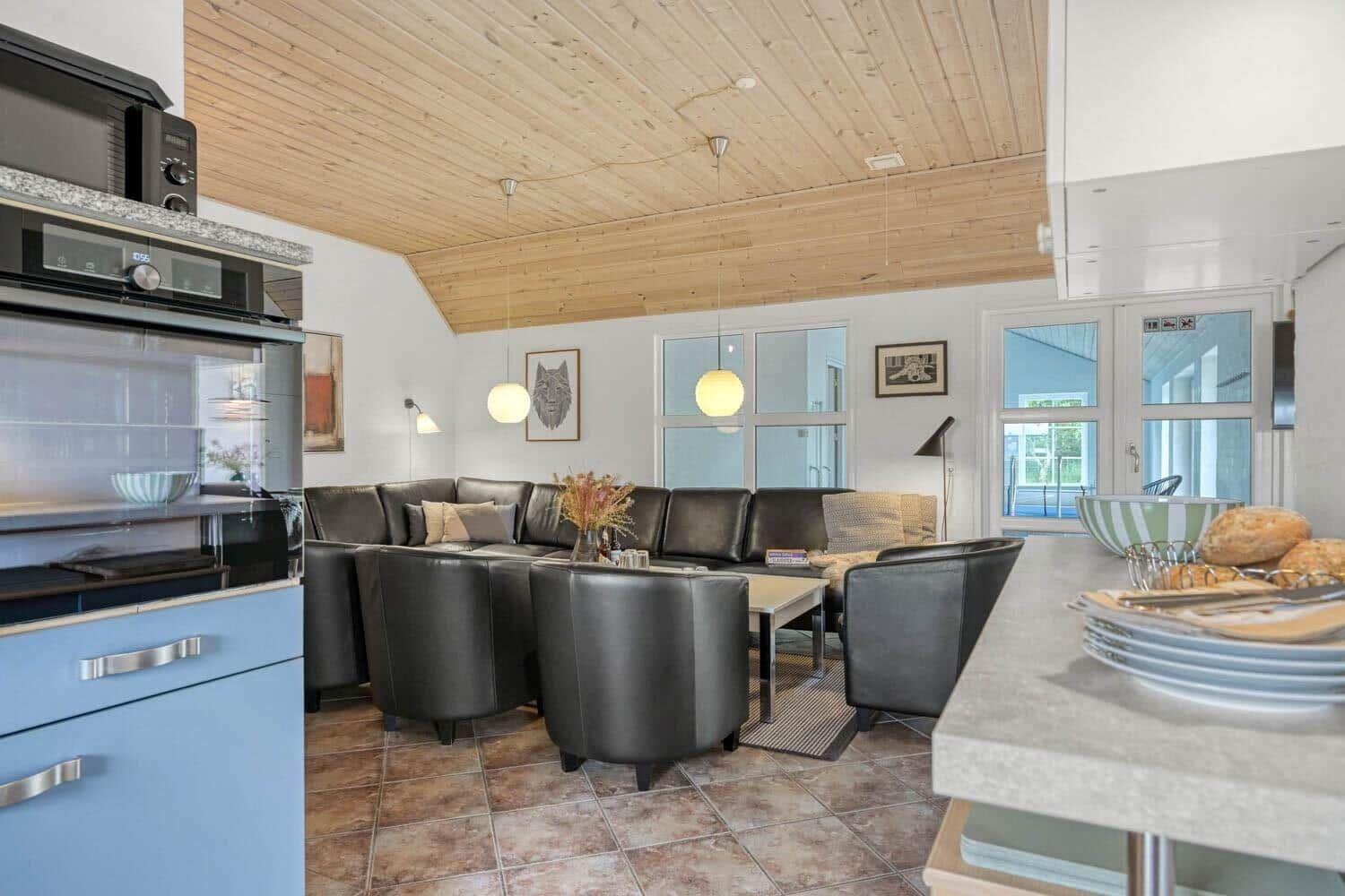 Wohnbereich mit Sofa, Stühlen und Küchenzeile unter Holzdecke.