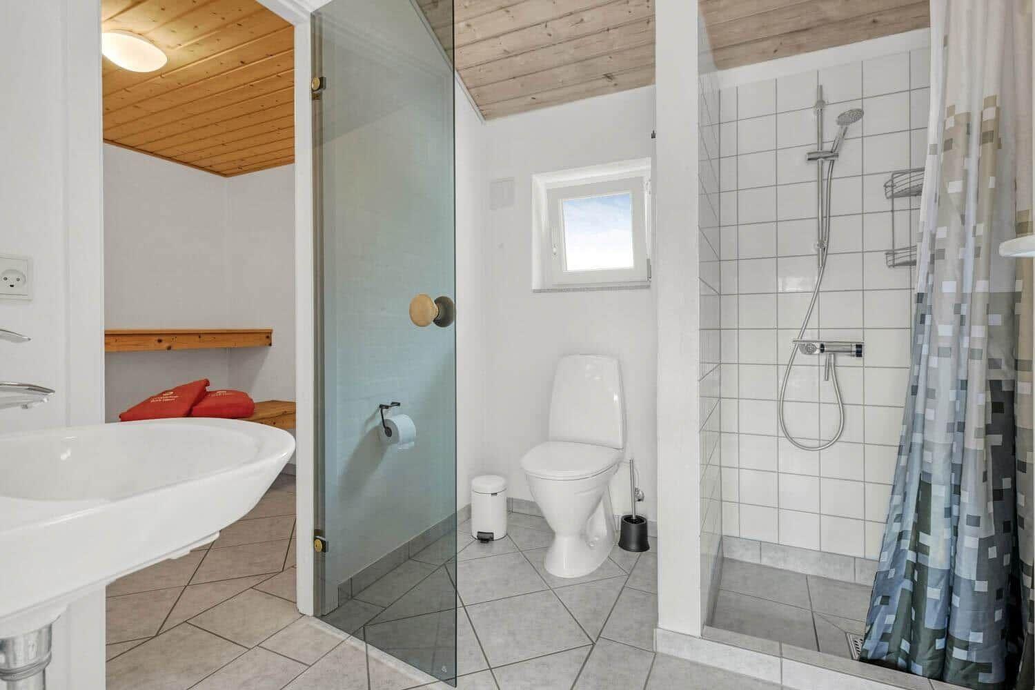 Bad mit Dusche, Toilette und Waschbecken. Holzdecke und Fenster sichtbar.