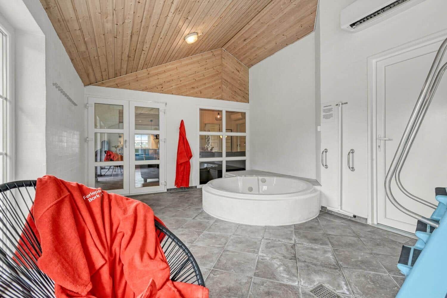 Rundes Whirlpoolbad mit Holzdecke und Glaswänden. Rote Bademäntel und Fliesenboden.
