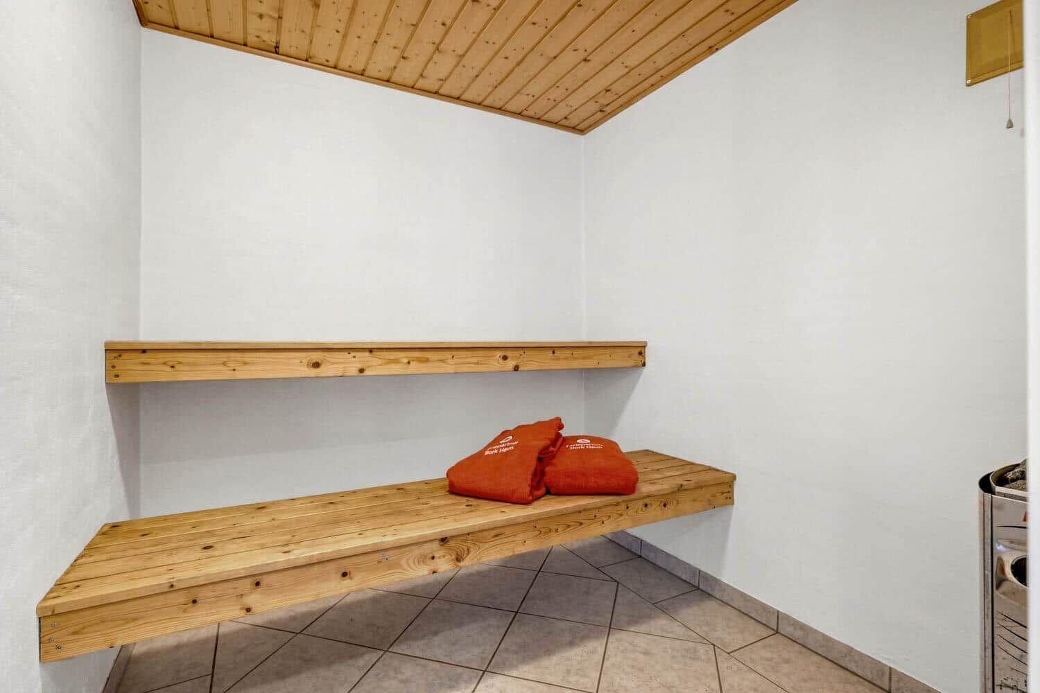 Sauna mit Holzbank und orangefarbenen Handtüchern an der Wand.