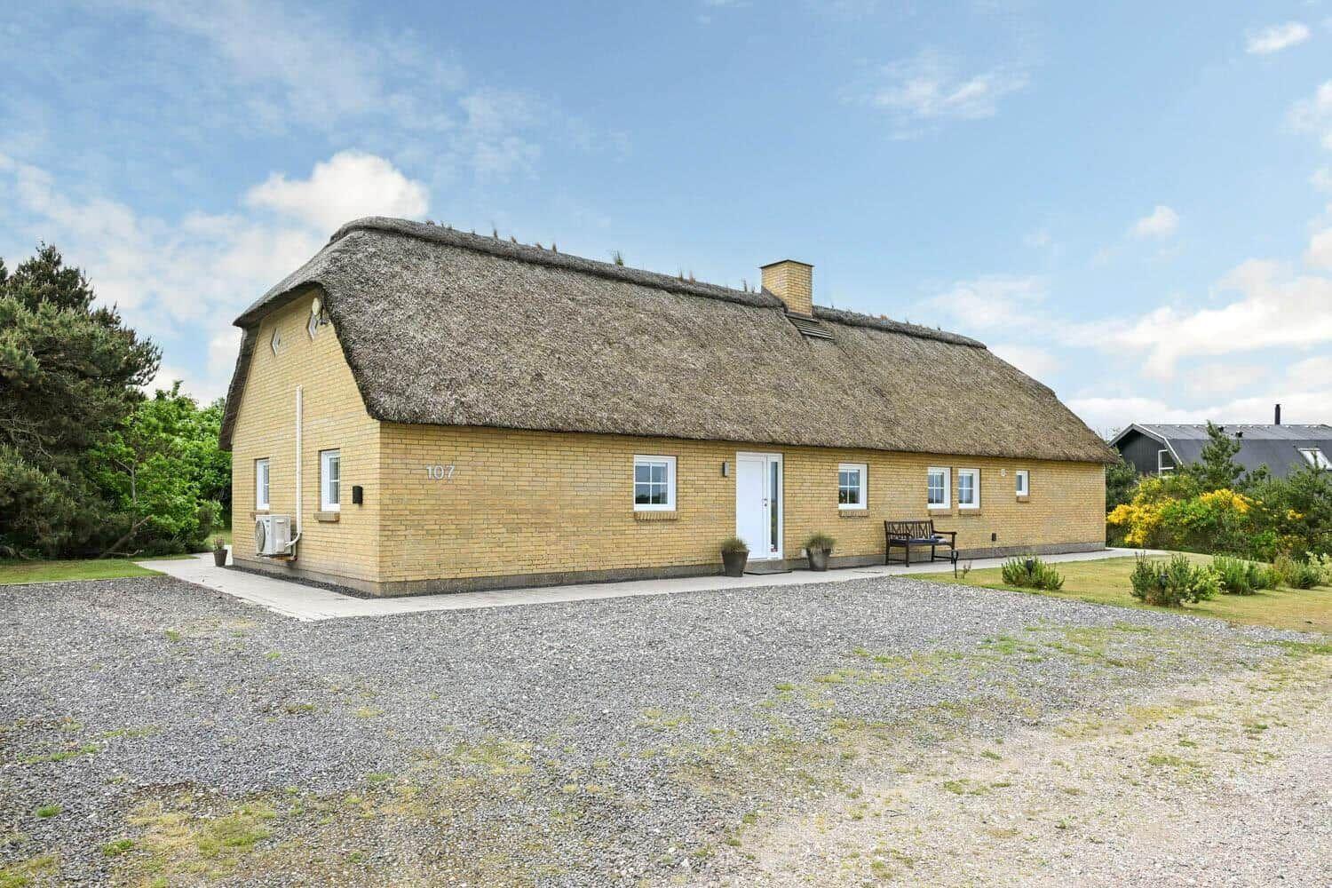 Ein gelbes Haus mit Strohdach, weißer Tür und Fenstern. Vorgarten mit Steinweg und Bank.