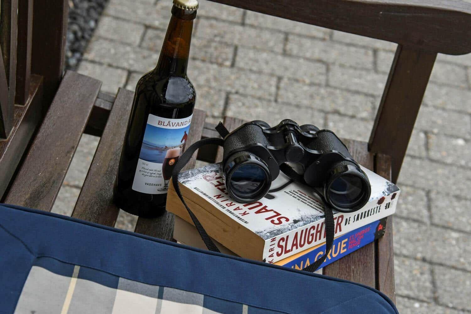 Eine Flasche Bier, ein Fernglas und Bücher auf einer Holzbank.