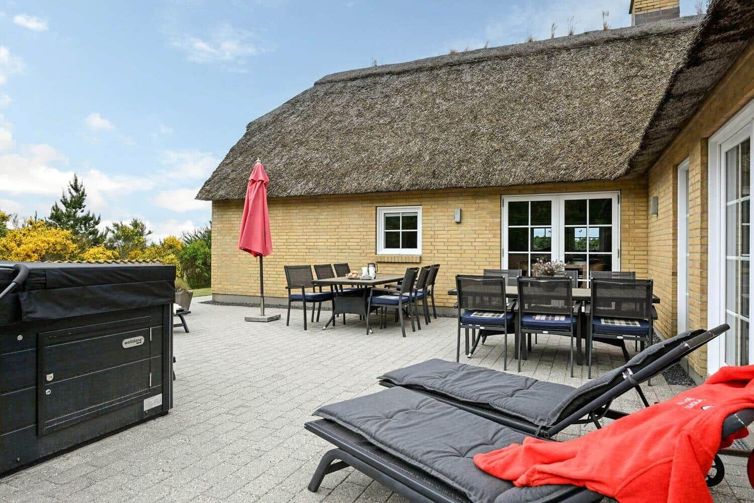 Terrasse mit Liegen, Tischen und Stühlen vor einem Haus mit Strohdach.