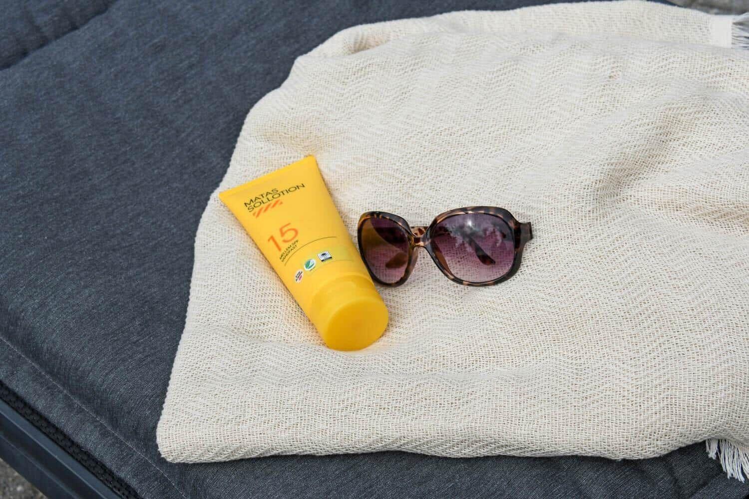 Sonnencreme und Sonnenbrille auf einem weißen Tuch.