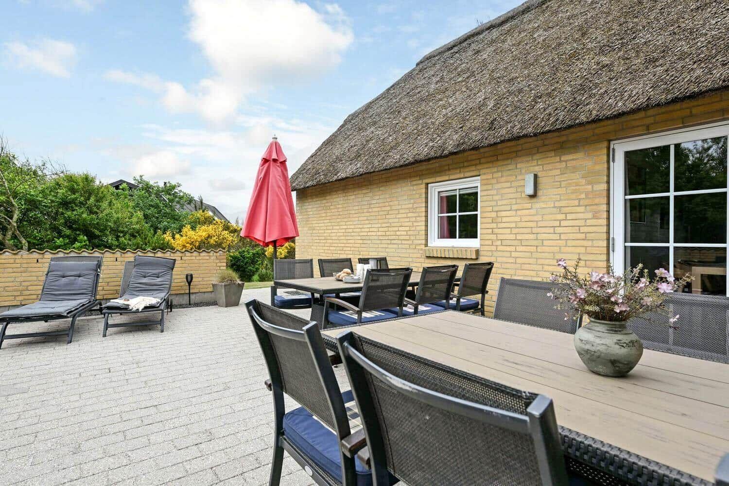 Terrasse mit Tisch, Stühlen und Liegestühlen vor einem Haus mit Strohdach.