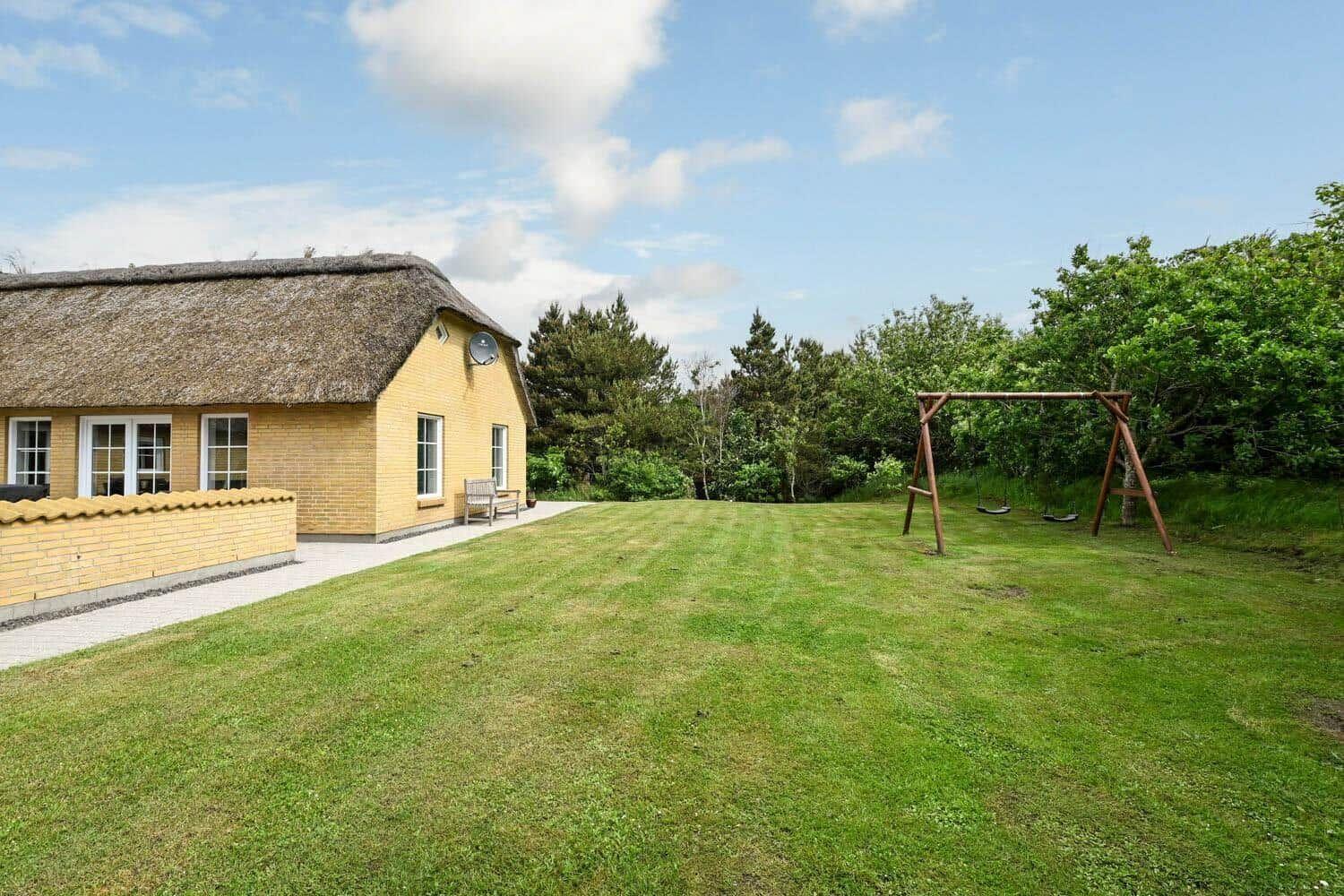 Haus mit Strohdach und großem Garten mit Schaukel.