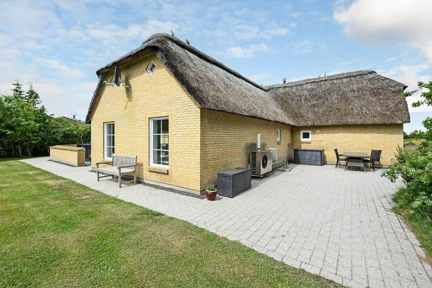 Haus mit Strohdach, Terrasse, Garten und Sitzgelegenheiten.