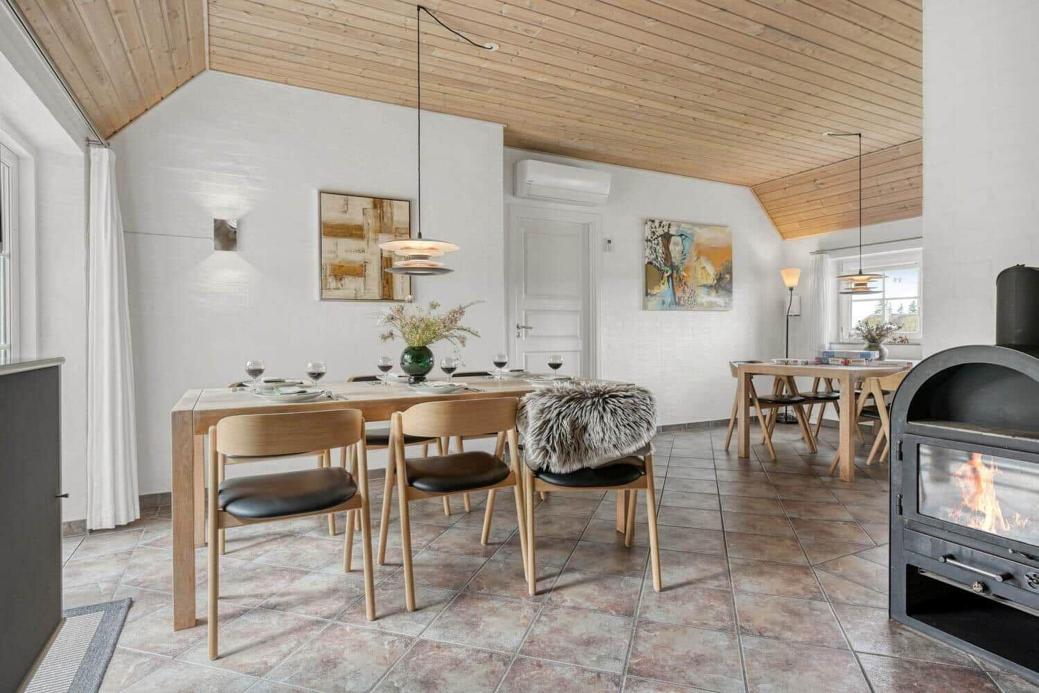 Esszimmer mit Holztisch, Stühlen und Kaminofen. Holzdecke und Wandgemälde.