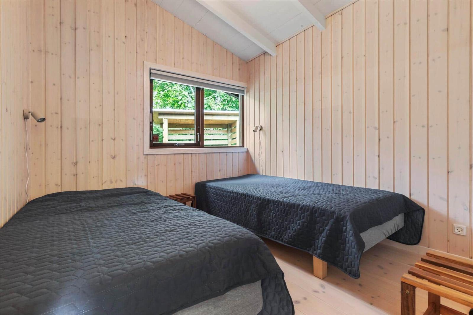 Two beds with dark covers in a room with wooden walls and a window.