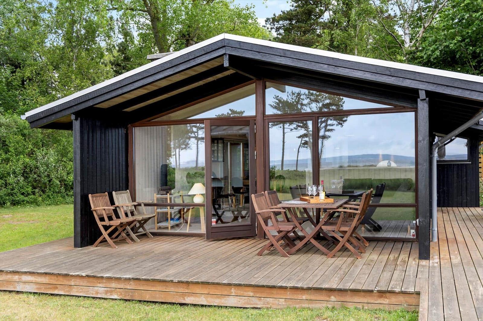 Modern cabin with wooden deck and large glass area. Furniture and table are outside.